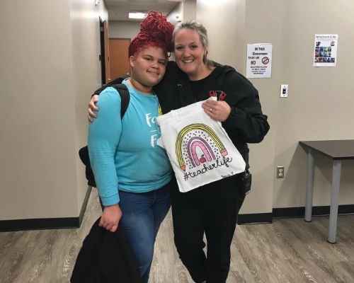  Student stands smiling with Mrs. Webb as she holds a decorated tote bag